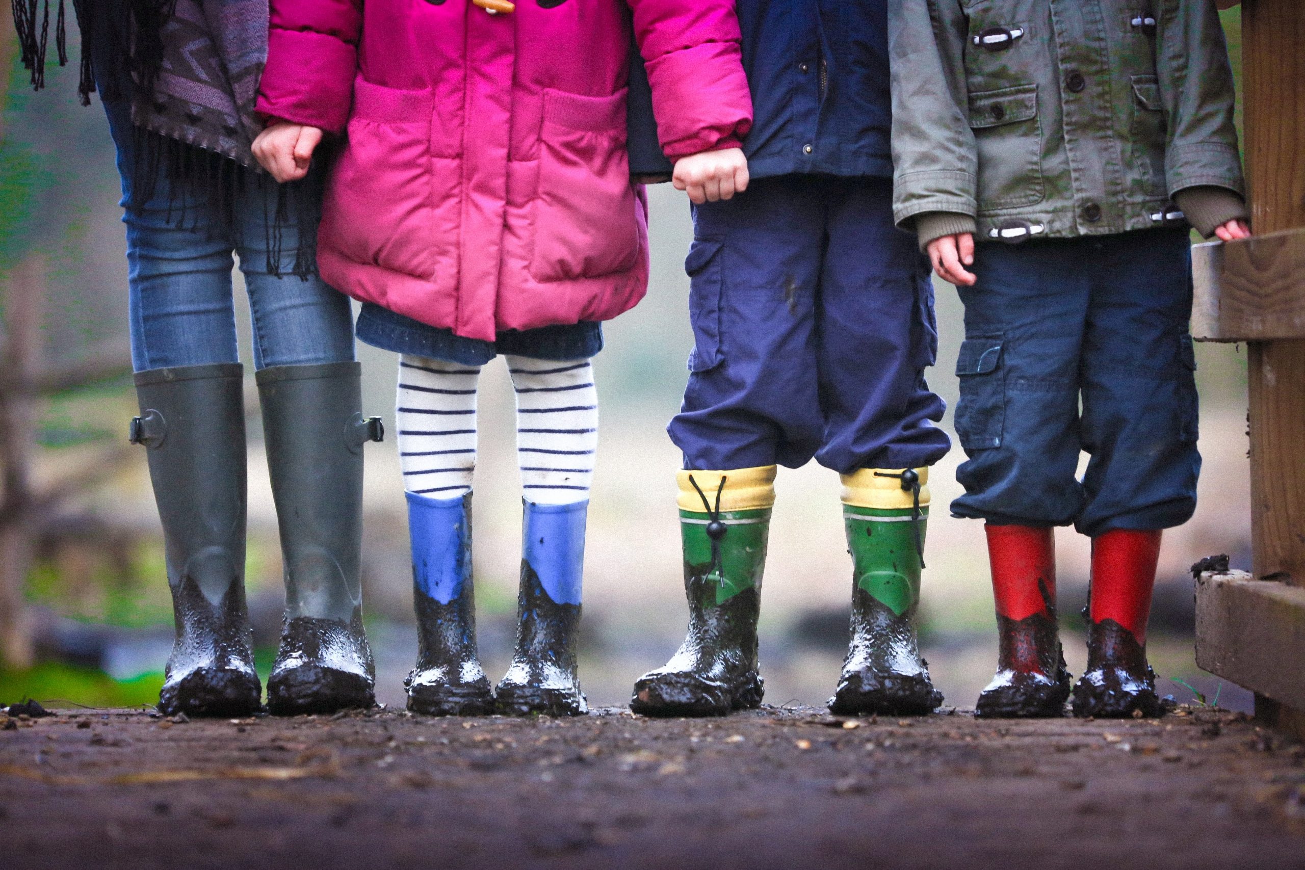 A group of kids standing outside together wearing rain boots