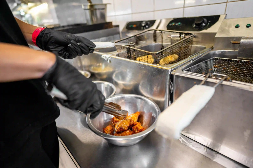 A restaurant worker fries chicken wings after changing the fryer oil.